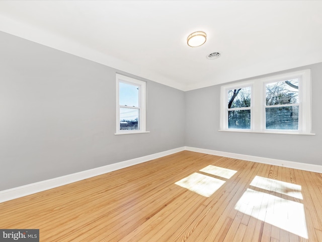 spare room featuring visible vents, baseboards, plenty of natural light, and wood finished floors