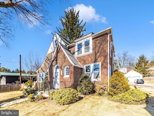 view of front of home with an outbuilding, fence, brick siding, and a shingled roof