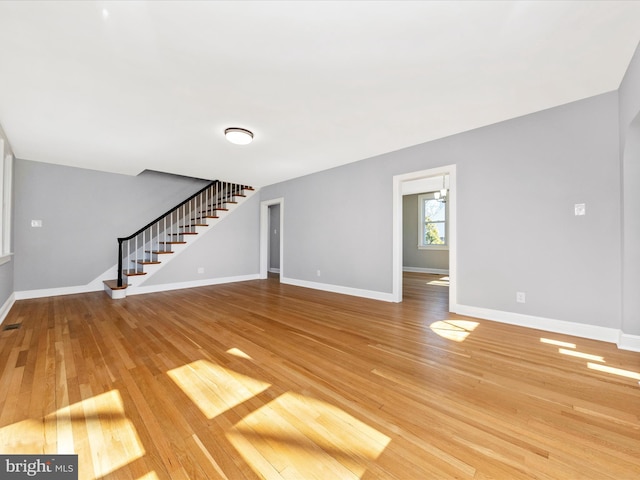 unfurnished living room with stairway, visible vents, light wood-type flooring, and baseboards