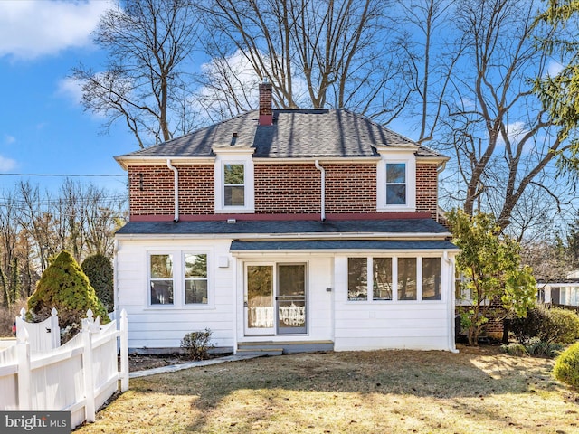 view of front of house featuring a front yard, fence, roof with shingles, a chimney, and brick siding