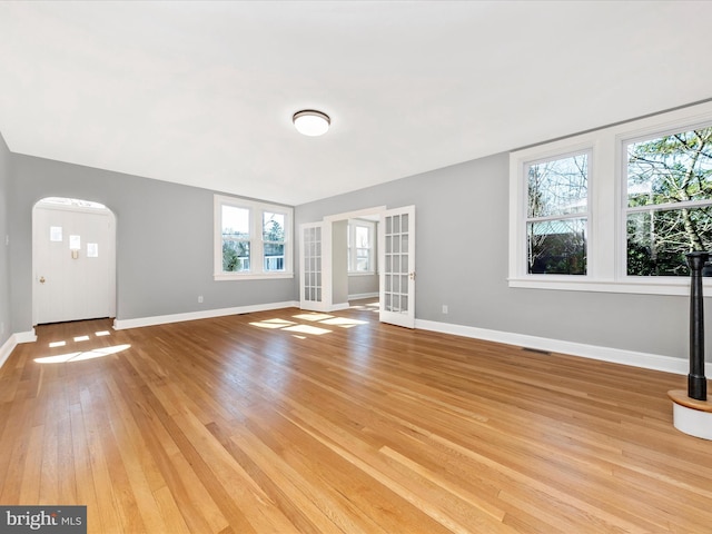 unfurnished living room featuring visible vents, baseboards, arched walkways, light wood-style floors, and french doors