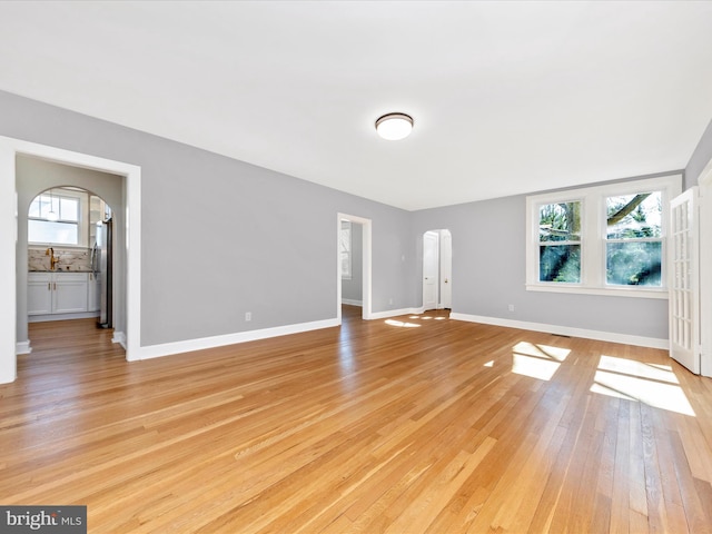 unfurnished living room with a sink, arched walkways, a healthy amount of sunlight, and light wood finished floors