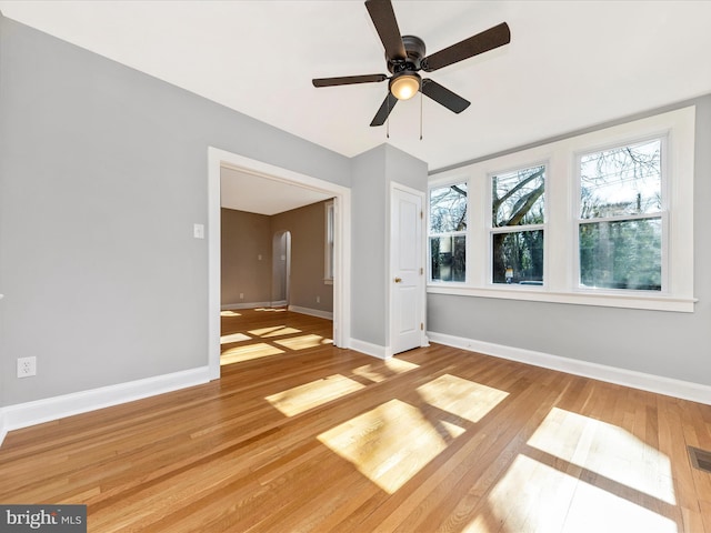 empty room with arched walkways, plenty of natural light, and wood-type flooring