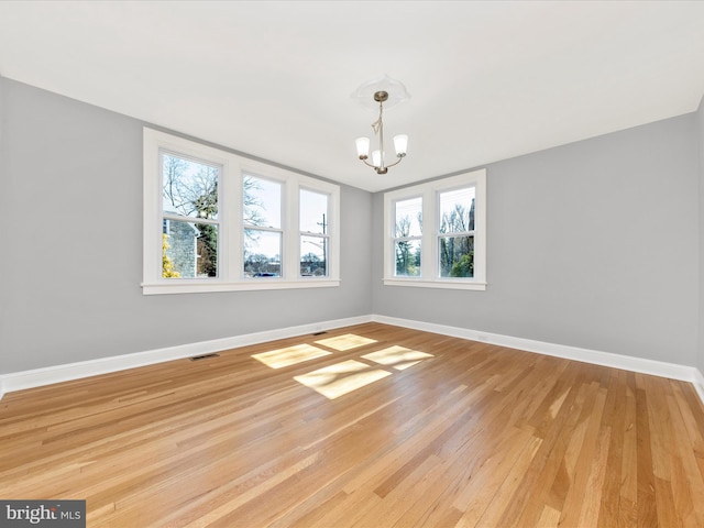 unfurnished room featuring light wood-style flooring, baseboards, a healthy amount of sunlight, and a chandelier