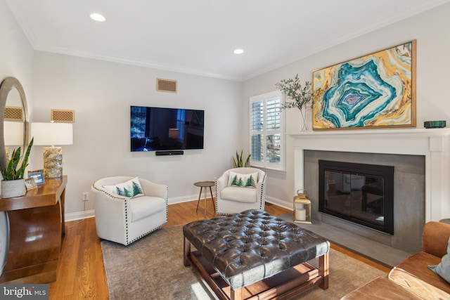 living room with wood finished floors, visible vents, baseboards, a fireplace with flush hearth, and crown molding