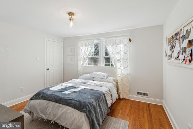 bedroom with wood finished floors, visible vents, and baseboards