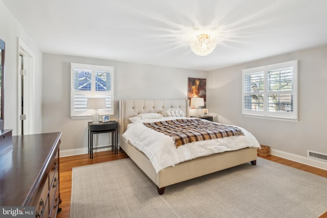 bedroom featuring visible vents, multiple windows, baseboards, and wood finished floors