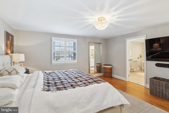 bedroom with a notable chandelier, baseboards, ensuite bath, and wood finished floors