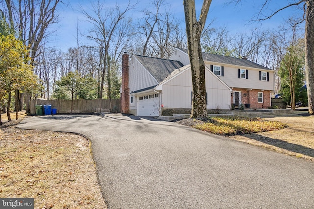 view of front of property featuring fence, driveway, an attached garage, a chimney, and brick siding