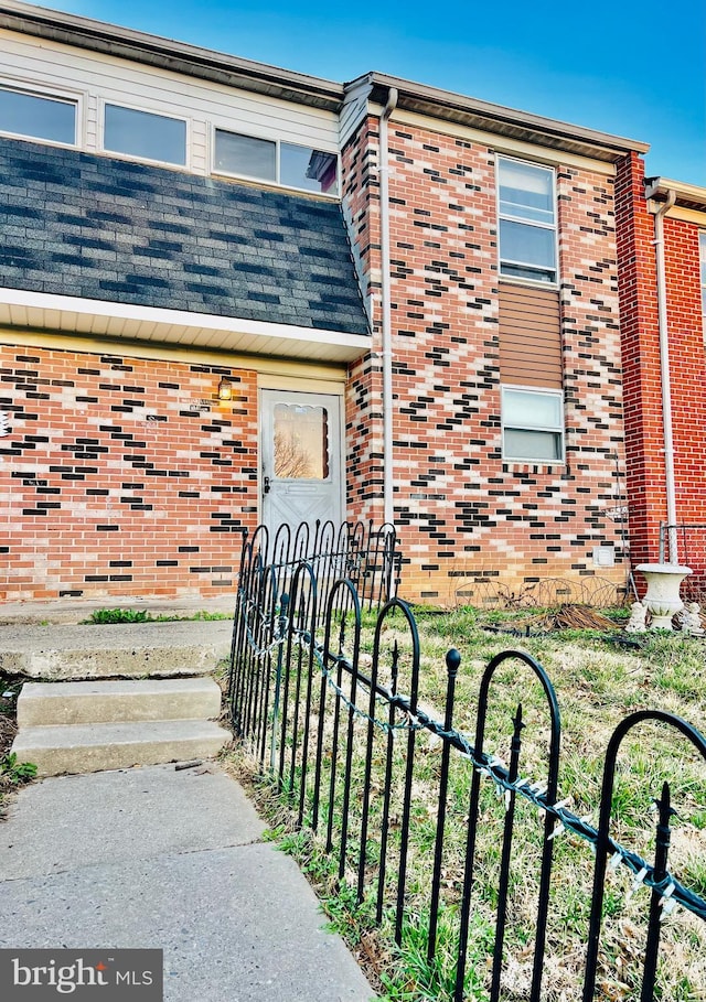 entrance to property with brick siding, roof with shingles, and fence