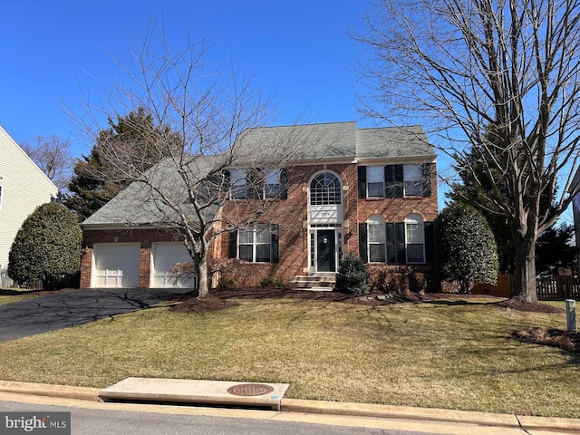 colonial inspired home featuring brick siding, an attached garage, aphalt driveway, and a front lawn