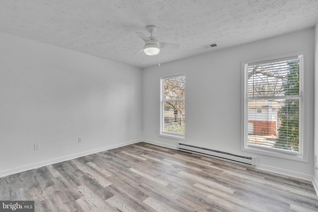 spare room featuring a baseboard heating unit, baseboards, visible vents, and wood finished floors