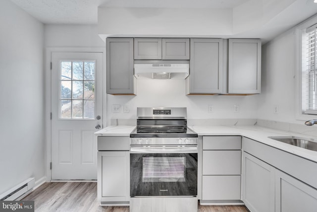 kitchen featuring stainless steel electric stove, a baseboard radiator, under cabinet range hood, and gray cabinetry