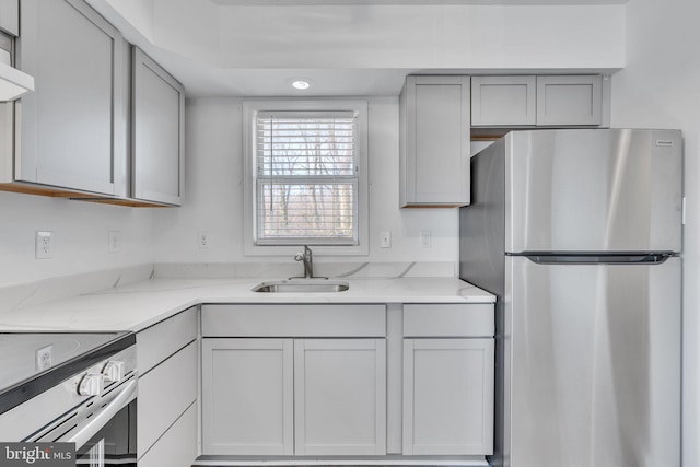 kitchen with light stone counters, gray cabinetry, freestanding refrigerator, and a sink