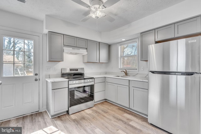 kitchen featuring gray cabinets, a sink, light countertops, under cabinet range hood, and appliances with stainless steel finishes