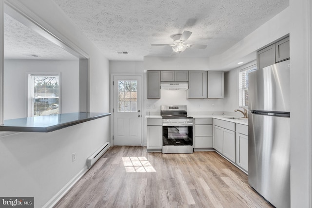 kitchen with a sink, gray cabinetry, under cabinet range hood, appliances with stainless steel finishes, and a baseboard radiator