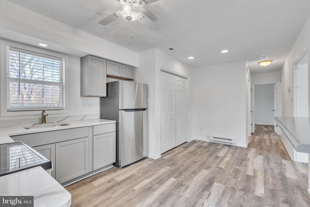 kitchen featuring visible vents, gray cabinetry, a sink, freestanding refrigerator, and baseboard heating