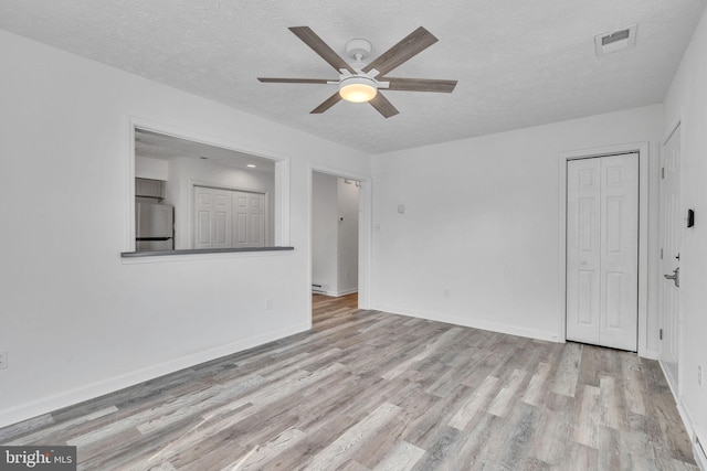 unfurnished room with baseboards, wood finished floors, visible vents, and a textured ceiling