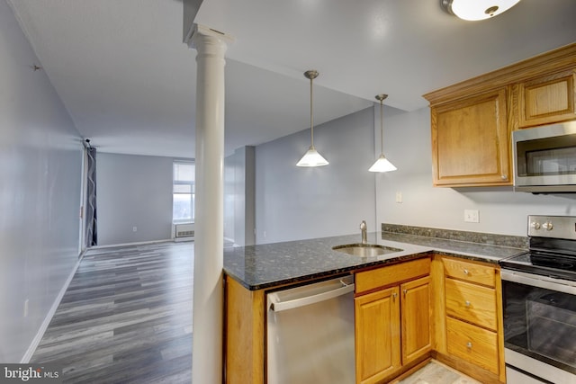 kitchen featuring a sink, dark stone counters, appliances with stainless steel finishes, light wood finished floors, and decorative columns