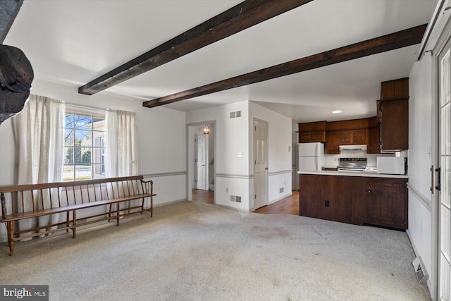 living area with beamed ceiling, light colored carpet, visible vents, and baseboards