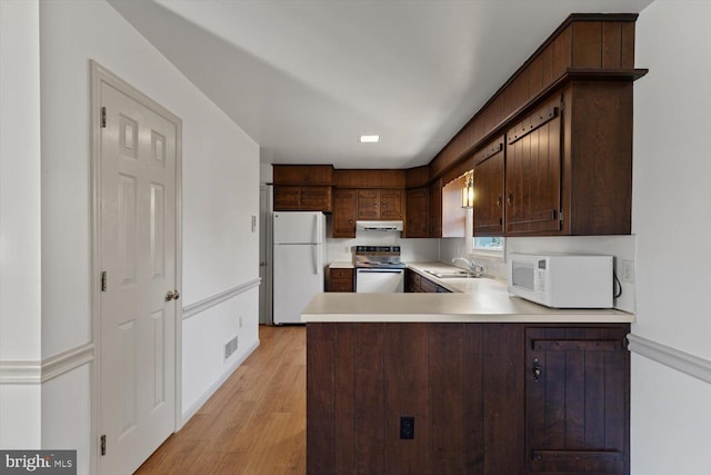 kitchen with white appliances, light wood finished floors, a peninsula, a sink, and light countertops