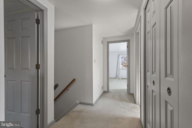 hallway with an upstairs landing, light carpet, and baseboards