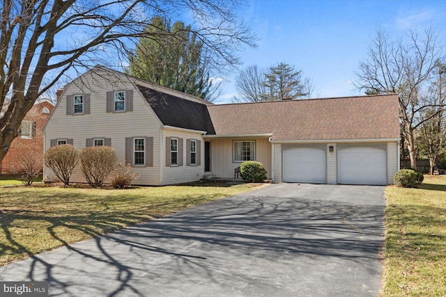 colonial inspired home featuring a front lawn, an attached garage, a gambrel roof, and driveway