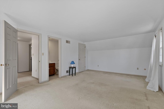 interior space featuring visible vents, light carpet, lofted ceiling, ensuite bathroom, and baseboards