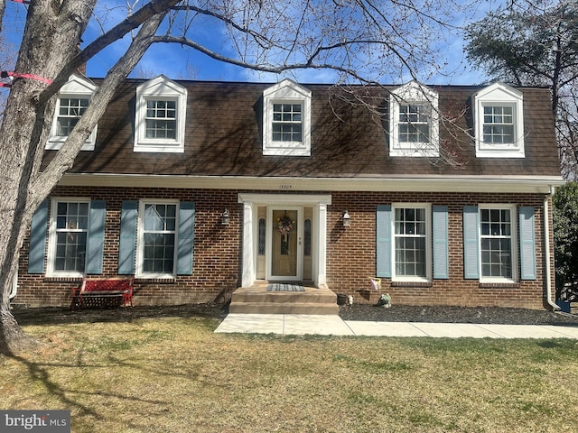 view of front of house featuring brick siding, a front yard, and a shingled roof