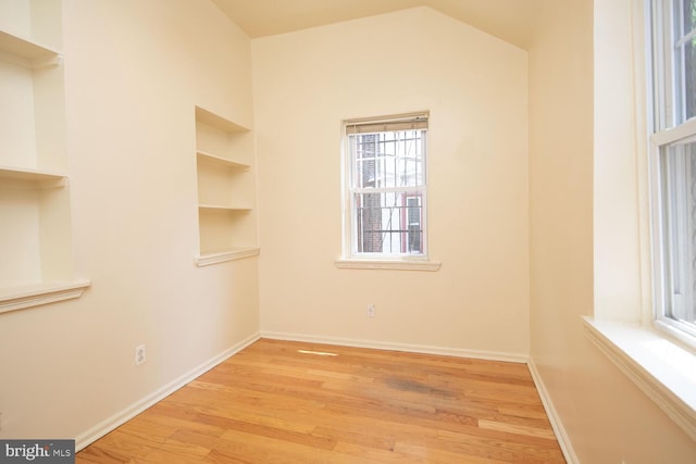 unfurnished room featuring vaulted ceiling, built in shelves, wood finished floors, and baseboards