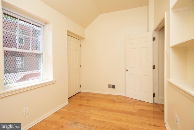 unfurnished bedroom featuring light wood-type flooring, visible vents, lofted ceiling, and baseboards