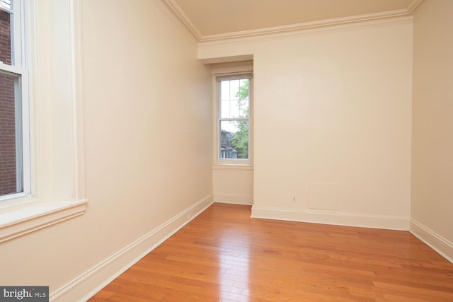 empty room featuring light wood-style flooring, crown molding, and baseboards