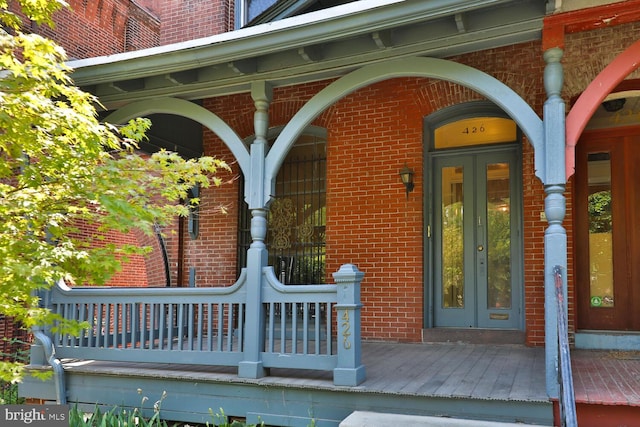 view of exterior entry with french doors, brick siding, and a porch