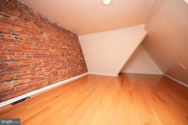 additional living space with wood finished floors, visible vents, brick wall, and baseboards