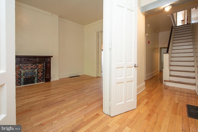 unfurnished living room featuring visible vents, stairs, ornamental molding, a fireplace, and wood-type flooring