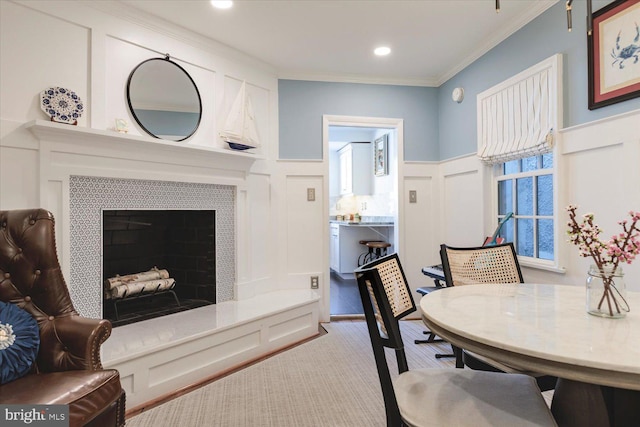 carpeted dining area featuring recessed lighting, ornamental molding, wainscoting, a tiled fireplace, and a decorative wall