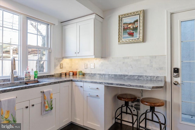 kitchen featuring tasteful backsplash, white cabinets, a kitchen bar, and a sink