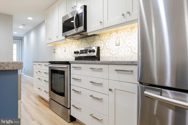 kitchen featuring backsplash, light stone countertops, light wood-style flooring, appliances with stainless steel finishes, and white cabinets
