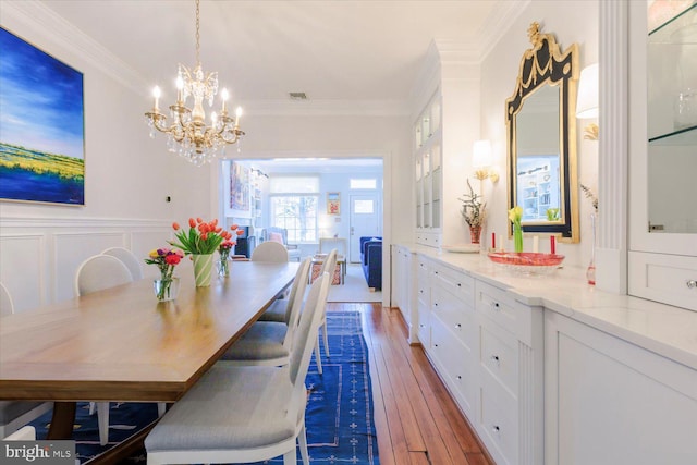 dining space with hardwood / wood-style floors, visible vents, a wainscoted wall, crown molding, and a notable chandelier
