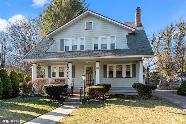 view of front of house featuring a front lawn, a chimney, covered porch, and a shingled roof