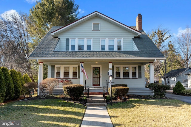 bungalow-style home featuring a chimney, covered porch, a front lawn, and a shingled roof