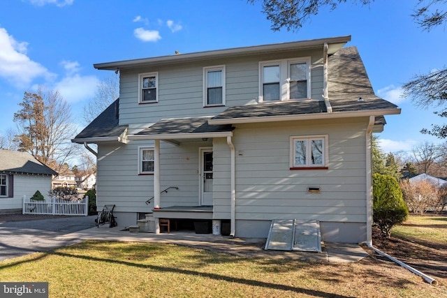 rear view of property featuring fence, a lawn, and roof with shingles