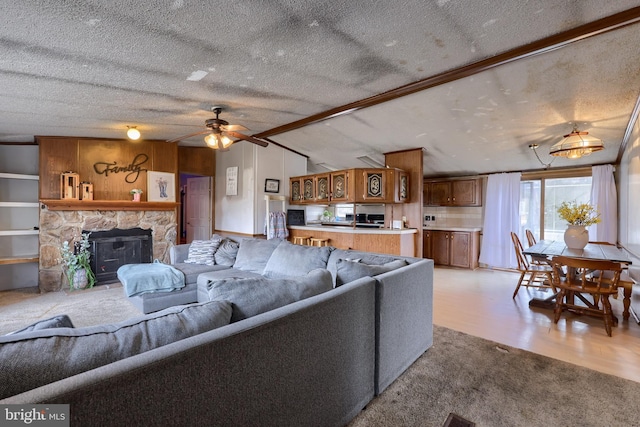 living room featuring vaulted ceiling with beams, ceiling fan, light wood-type flooring, a fireplace, and a textured ceiling