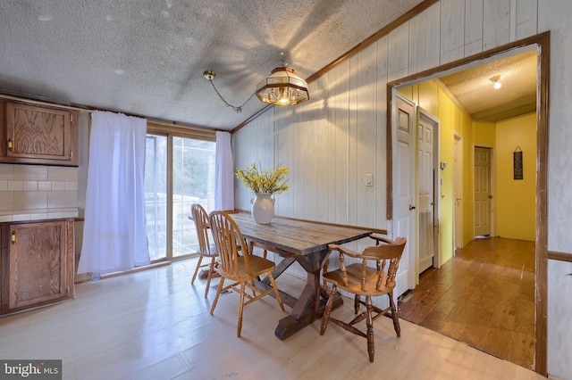 dining space featuring light wood-style flooring, ornamental molding, and a textured ceiling