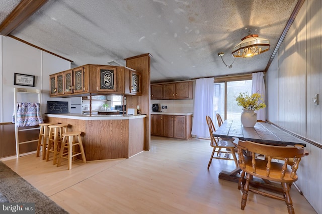 kitchen with a peninsula, light wood-style flooring, vaulted ceiling with beams, and a textured ceiling