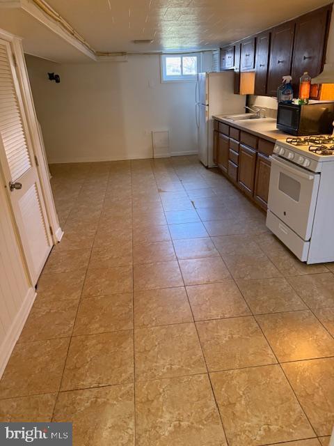 kitchen with light tile patterned floors, white range with gas cooktop, a sink, light countertops, and black microwave