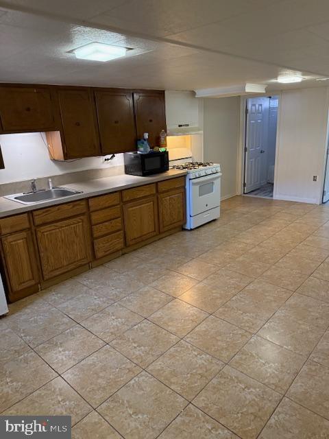 kitchen featuring brown cabinetry, black microwave, gas range gas stove, and a sink