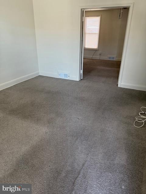 spare room with baseboards, visible vents, and dark carpet