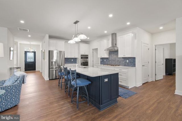 kitchen with visible vents, wall chimney range hood, a kitchen bar, appliances with stainless steel finishes, and dark wood-style floors