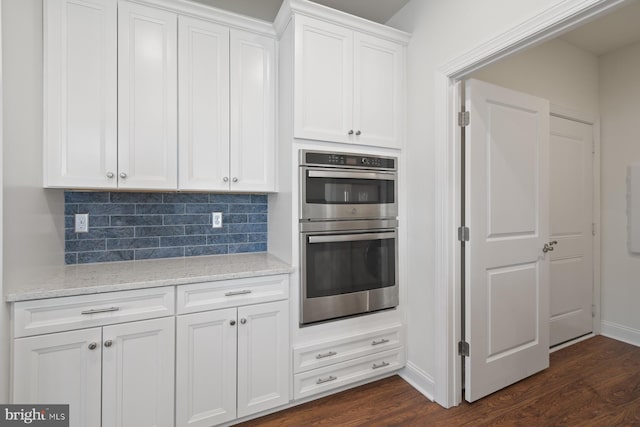 kitchen with light stone counters, tasteful backsplash, dark wood finished floors, double oven, and white cabinets